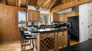 A wooden cabin-style kitchen with a large island, bar stools, and a black refrigerator. - ~Fireworks On The 3rd~Sunrise Vista~Lakefront~Dock~Kayaks~Hot Tub~Games~NEW AC~ (Gaylord)