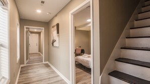 A hallway with wooden flooring, a staircase, and a bedroom with a bed and a desk. - Newly renovated 4BR CozySuites (Louisville)
