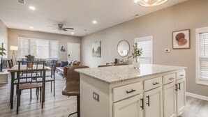 A spacious kitchen with a large island, wooden dining table, and chairs, and a ceiling fan. - Newly renovated 4BR CozySuites (Louisville)