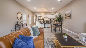 A modern living room with a leather sofa, a coffee table, and a dining area with chairs and a table. - Newly renovated 4BR CozySuites (Louisville)
