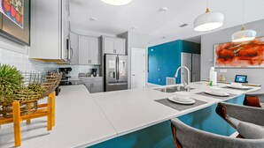 A modern kitchen with white cabinets, a large island, and a blue accent wall. - New - Sleeps 21 - Champions Gate Hyperdrive House (Kissimmee)