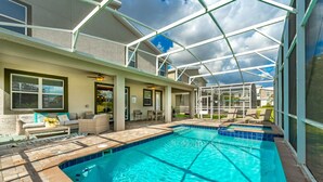 A swimming pool with a glass enclosure, a patio area with outdoor furniture, and a covered entryway. - New - Sleeps 21 - Champions Gate Hyperdrive House (Kissimmee)