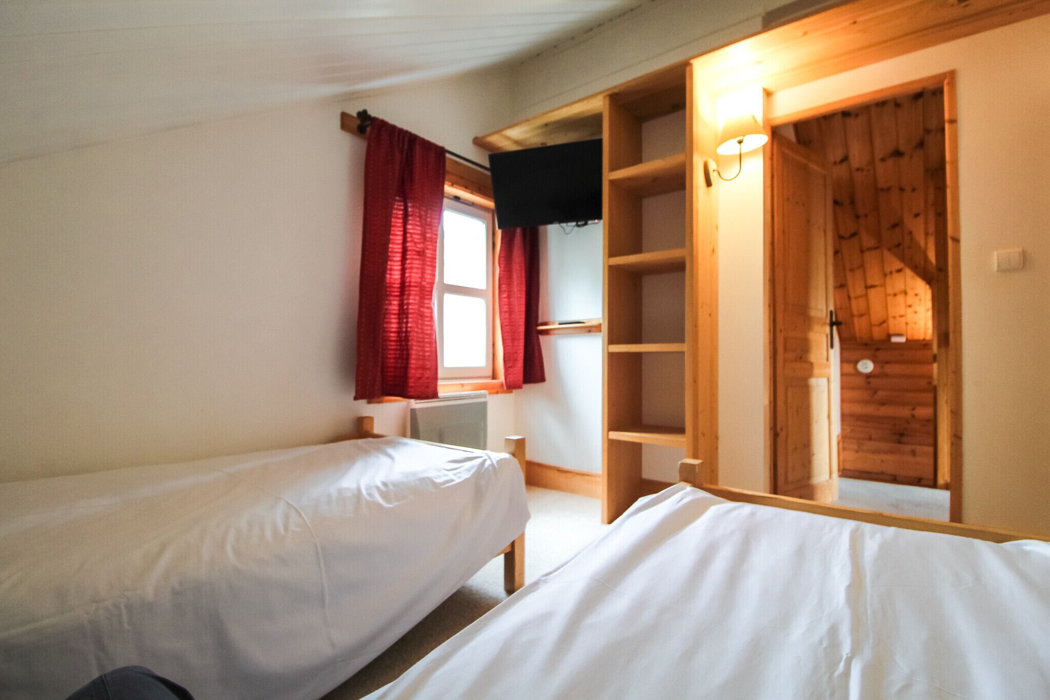 Una camera da letto con due letti, una finestra con tende rosse, un'armadio in legno e una mensola a incasso.