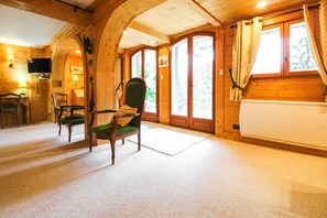 Un interior de madera con una silla verde, un sofá, un televisor y una ventana con cortinas.