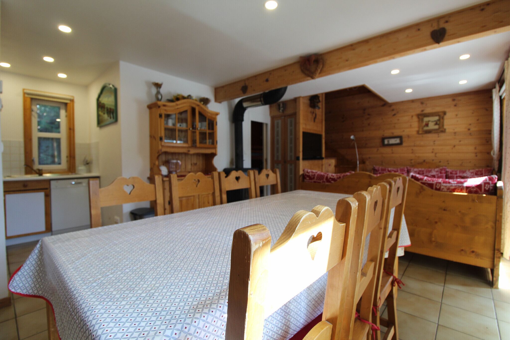 A dining area with a table set for four, wooden chairs, a cabinet with glass doors, and a kitchen in the background.