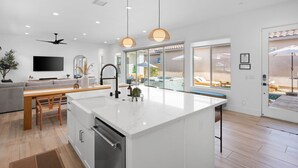 A modern kitchen with a large island, wooden dining table, and pendant lighting. - Private pool & hot tub - PGA West retreat (La Quinta)