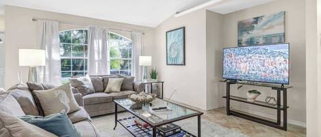 A living room with a sofa, coffee table, TV, and artwork.