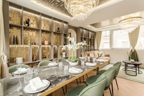 A modern dining area with a long table set for six, surrounded by green upholstered chairs.
