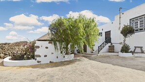 Um edifício branco com uma parede de pedra, uma árvore e uma escadaria que leva a uma porta.