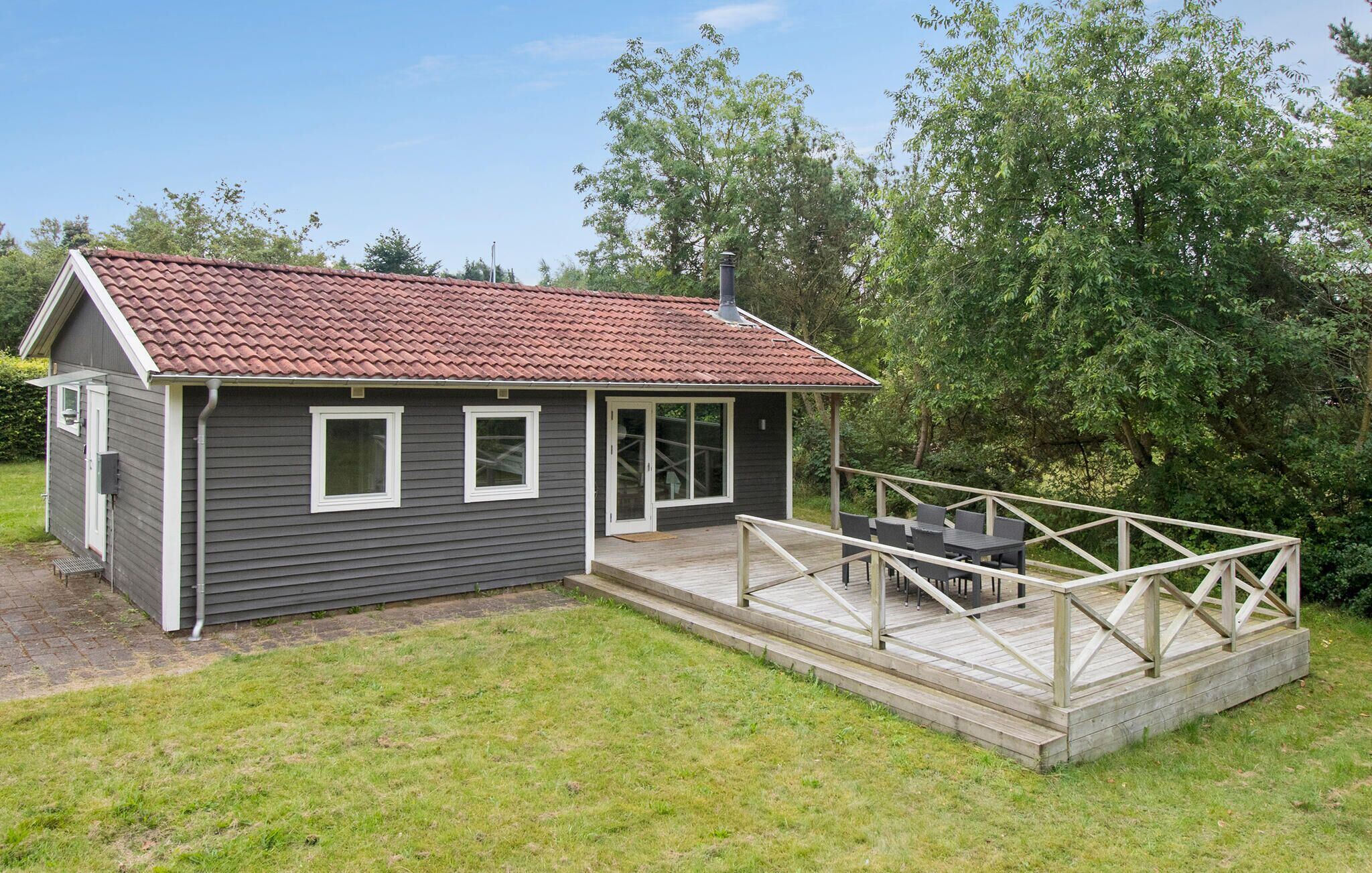 Een klein, gelijkvloers huis met een rode dakbedekking, een veranda met een leuning en een klein terras.