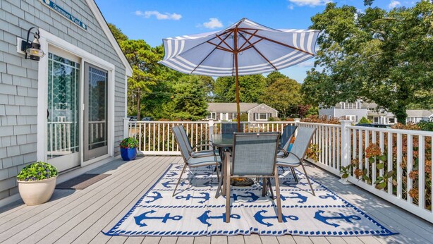 Eine Terrasse mit Tisch, Stühlen, einem großen Sonnenschirm und einem dekorativen Teppich mit Anker-Muster.