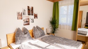 A double bed with grey linens and branch-patterned pillows, a bedside table with a lamp, a green plant, and wall art depicting nature scenes.