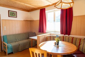 Una habitación acogedora con techo de madera, un sofá, una mesa con sillas y un ventanal con cortinas rojas.
