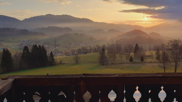 A mountainous landscape with a village and a sunset.