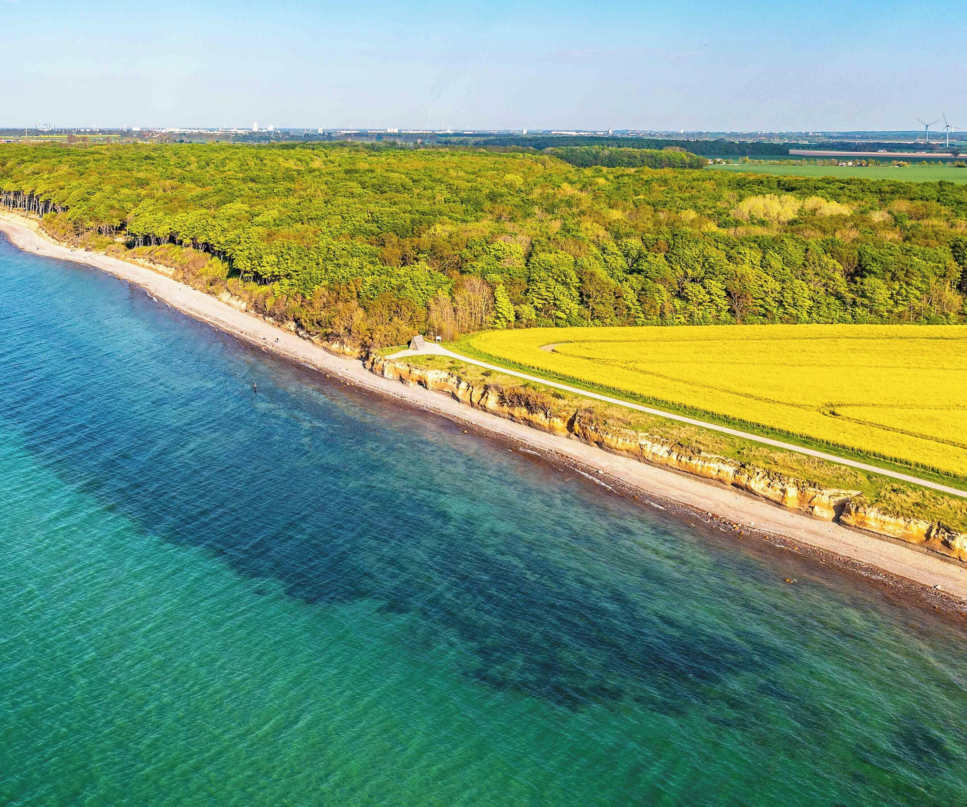 An aerial view of a coastal area with a beach, a road, and a field.