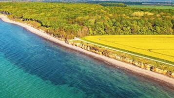 An aerial view of a coastal area with a beach, a road, and a field.