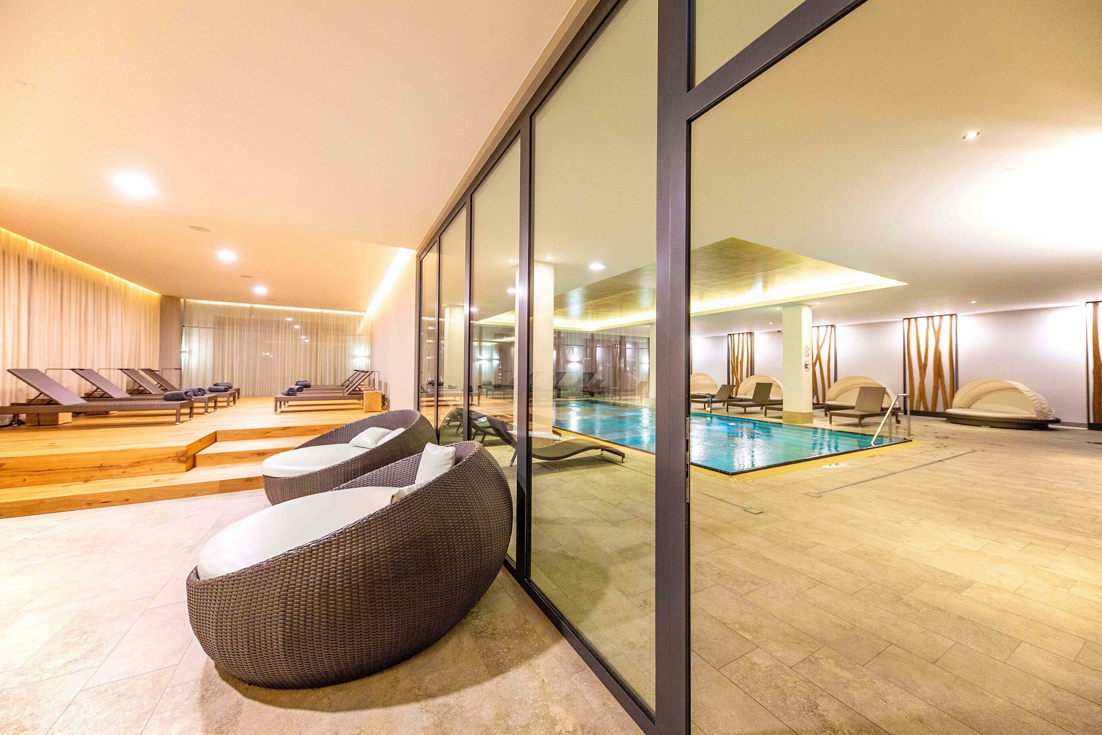 Un espace piscine intérieur moderne, doté de chaises longues, d’une piscine et d’un mur en verre.