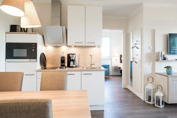 A modern kitchen with white cabinets, a microwave, a coffee maker, and a dining area with a wooden table and chairs.