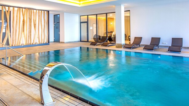 An indoor swimming pool with a water fountain, lounge chairs, and a modern interior design. - Apartment 'Waterkant 2-50' with Sea View, Balcony and Wi-Fi (Börgerende-Rethwisch)