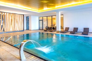 An indoor swimming pool with a water fountain, lounge chairs, and a modern interior design.