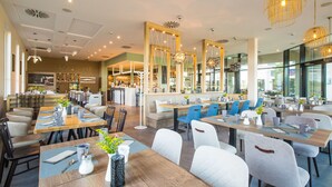 A modern restaurant with wooden tables, blue and white chairs, and pendant lighting. - Apartment 'Waterkant 2-50' with Sea View, Balcony and Wi-Fi (Börgerende-Rethwisch)