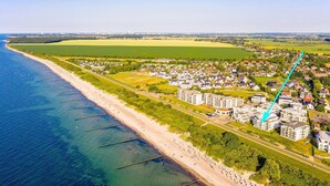An aerial view of a coastal area with a beach, residential buildings, and wind turbines in the distance. - Apartment 'Villa Deichgraf 07 Ostseeblick' with Sea View, Balcony and Wi-Fi (Börgerende-Rethwisch)