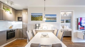 A modern kitchen with a dining area, a coffee machine, and a TV displaying an advertisement. - Apartment 'Villa Deichgraf 07 Ostseeblick' with Sea View, Balcony and Wi-Fi (Börgerende-Rethwisch)