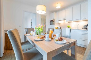 Une cuisine moderne avec des meubles blancs, une table à manger en bois et un coin repas pour le petit-déjeuner.