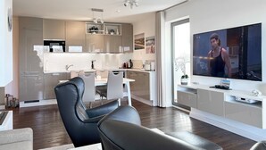 A modern living room with a flat-screen TV, a dining area with a white table and chairs, and a kitchen with stainless steel appliances. - Apartment 'Villa Deichgraf 12 Meerblick' with Sea View, Balcony and Wi-Fi (Börgerende-Rethwisch)