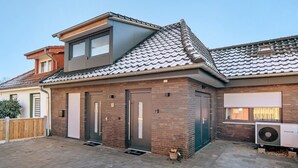 Une maison moderne à deux étages, avec un toit en tuiles, une façade en briques et une porte de garage.