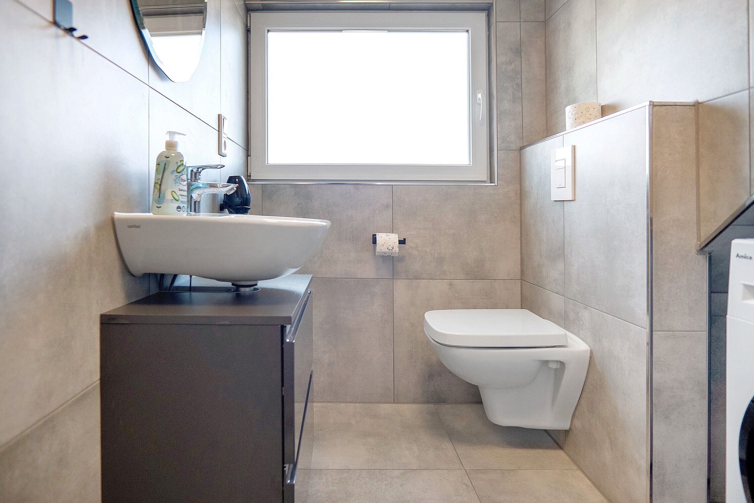 Ein Badezimmer mit einem weißen Waschbecken, einer Toilette und einem Fenster über der Toilette.