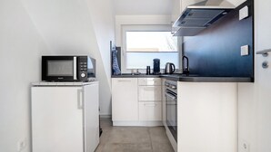 Une cuisine compacte équipée d’un four à micro-ondes, d’un réfrigérateur, d’une cuisinière et d’une fenêtre avec des stores.