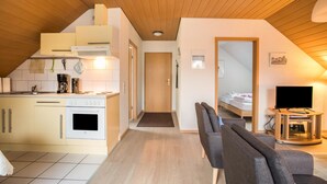 Una cocina compacta con estufa, horno y microondas, un comedor con mesa y sillas, y un dormitorio con cama y televisor.