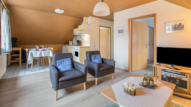 Una sala de estar moderna con dos sillones grises, una mesa de comedor con sillas, un televisor y un techo de madera.