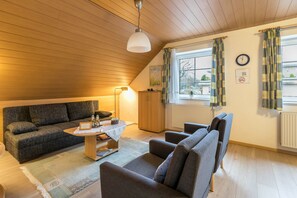 A cozy loft-style living room with a high ceiling, a sofa, armchairs, a coffee table, and a lamp. - Apartment 'Ferienwohnung Frischauf' with Private Terrace, Private Garden and Wi-Fi (Flensburg)