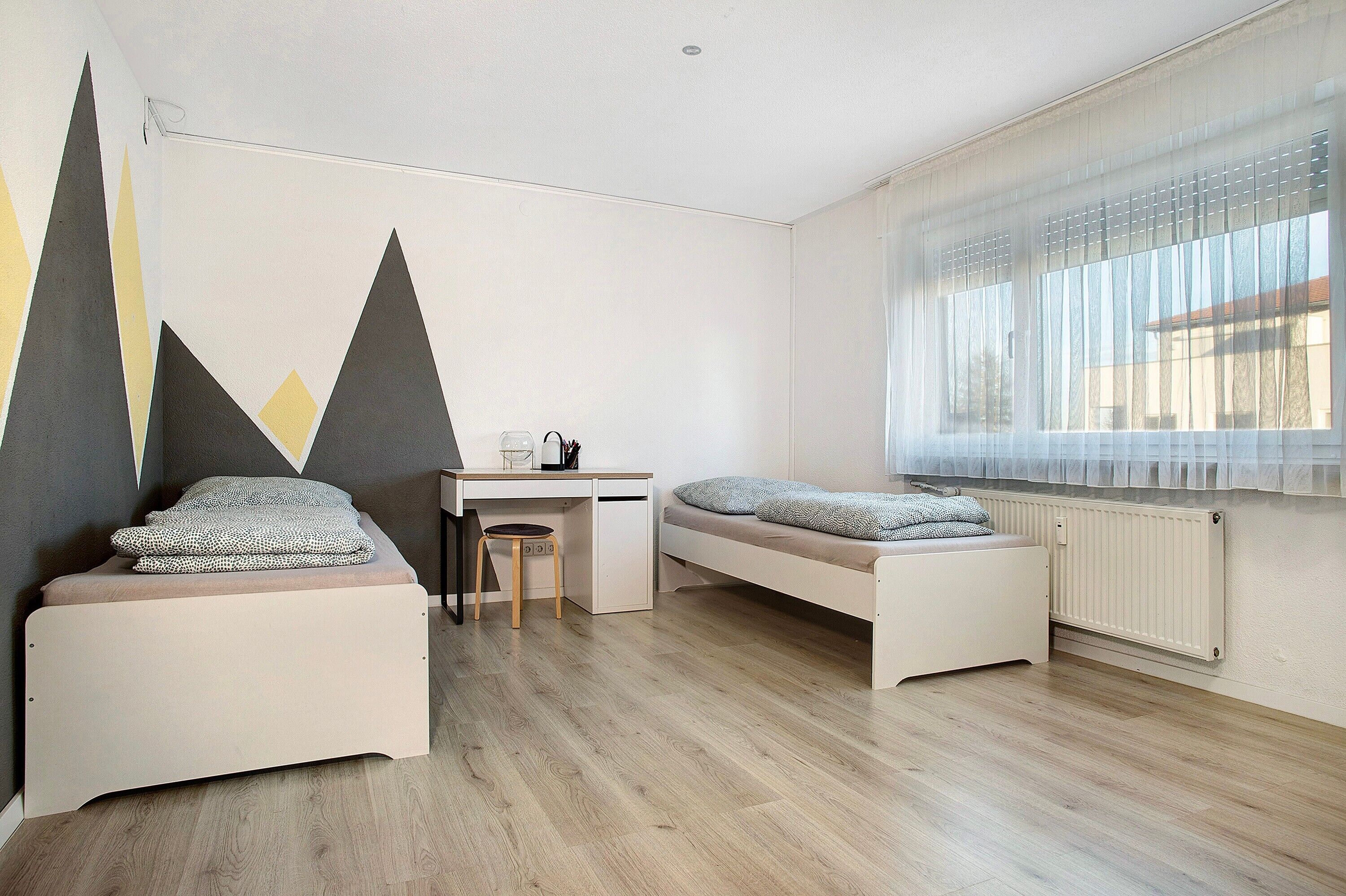 Una habitación con dos camas, un escritorio, una silla y un radiador.