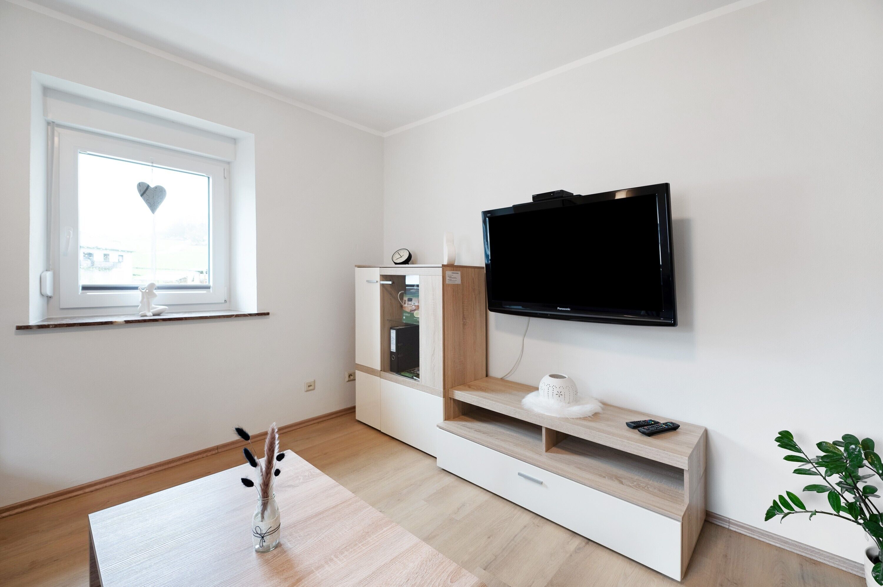 A modern living room with a flat-screen TV mounted on the wall, a wooden coffee table, and a small plant.