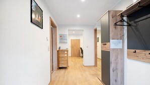 Un couloir avec un plancher en bois, une commode en bois, un tableau encadré accroché au mur et une porte avec une pancarte.