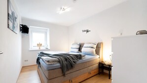 Une chambre à coucher avec un lit, une fenêtre, une table de chevet et un téléviseur fixé au mur.