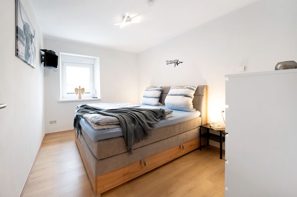 A bedroom with a bed, a window, a bedside table, and a wall-mounted TV.