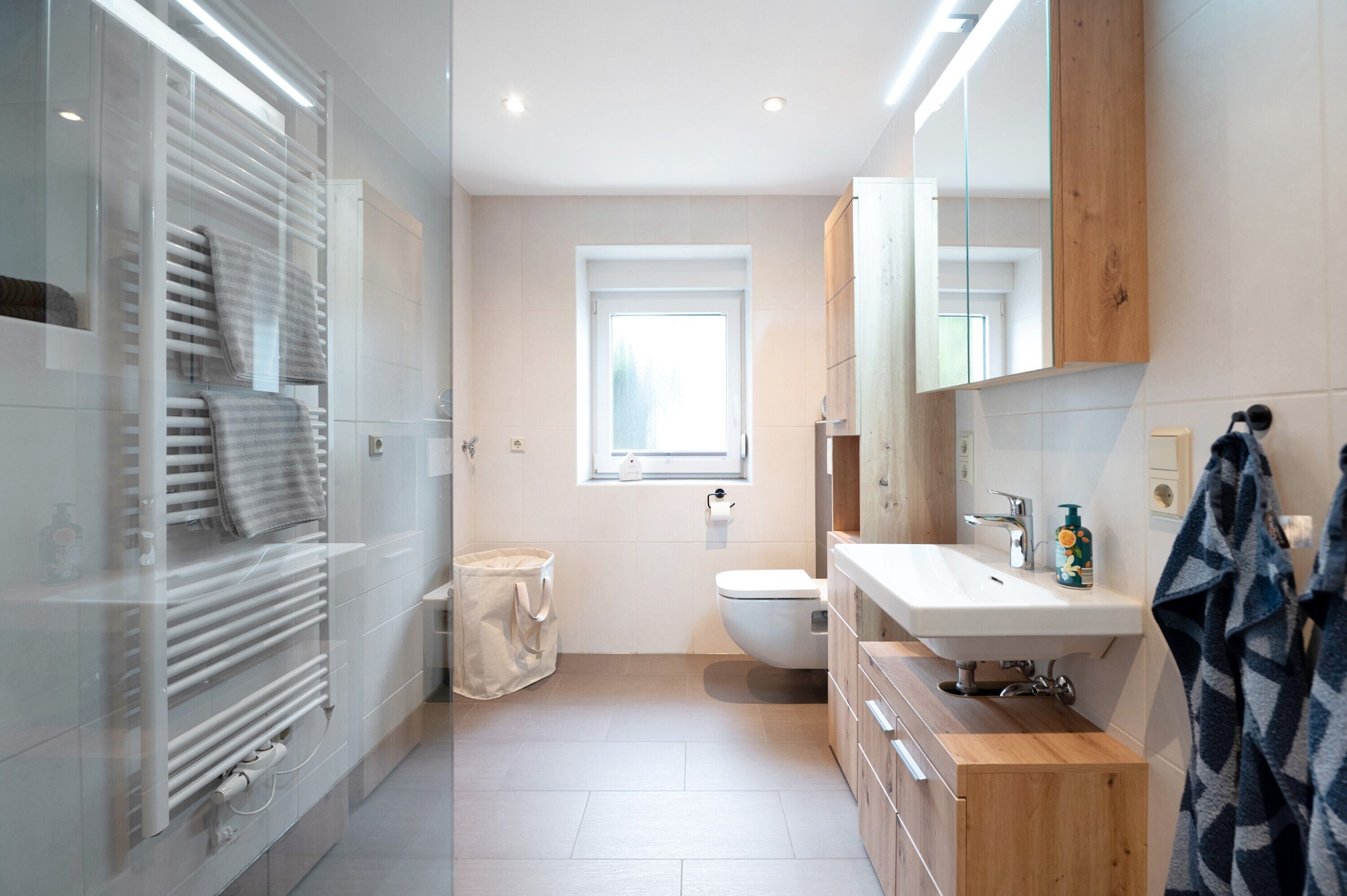 Ein modernes Badezimmer mit einer Duschkabine aus Glas, einer weißen Toilette, einem Holzwaschtisch und einem großen Spiegel.