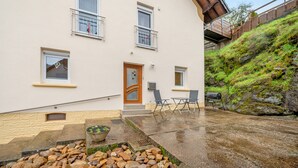 Un bâtiment à deux étages doté d’une porte en bois, de fenêtres et d’un petit espace extérieur aménagé avec des chaises et un barbecue.