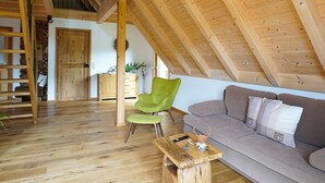 A loft-style room with a sloped ceiling, wooden beams, a sofa, a green chair, a wooden coffee table, and a staircase. - Apartment 'Heimatglück 2, Maisonette, 76qm' with Shared Terrace, Balcony and Wi-Fi (Lautenbach)
