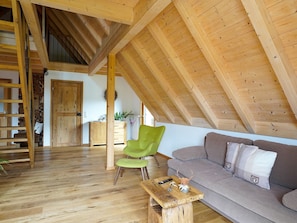 Une pièce de style « loft », avec un plafond en pente, des poutres en bois, un canapé, un fauteuil vert, une table basse en bois et un escalier.