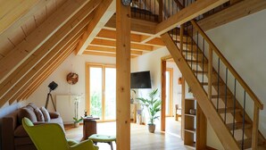 A spacious loft with a wooden staircase, a sofa, a green chair, a table, and a TV. - Apartment 'Heimatglück 2, Maisonette, 76qm' with Shared Terrace, Balcony and Wi-Fi (Lautenbach)
