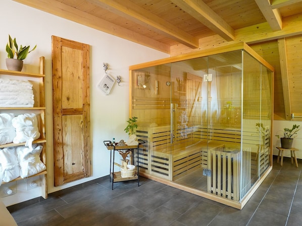 Un sauna avec des poutres en bois, une paroi en verre et un banc en bois.