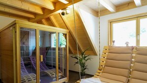 Interno in legno con sauna vetrata, una poltrona a dondolo in legno e un'ampia finestra.