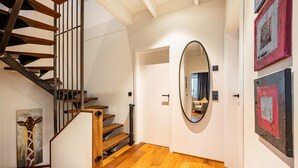 Un escalier avec des marches en bois et des rampes en métal, un grand miroir rond accroché au mur et des œuvres d’art.