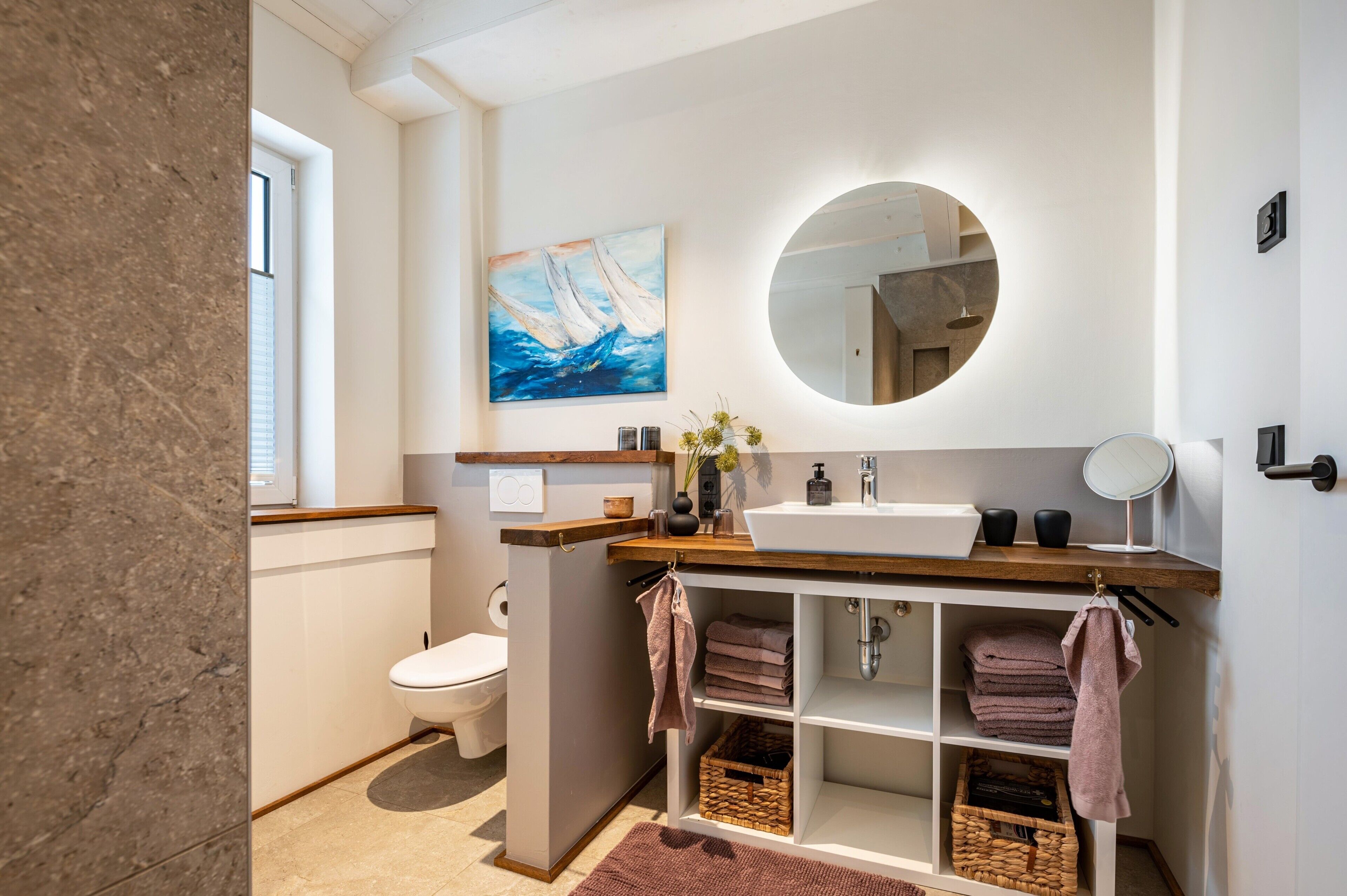 A modern bathroom with a toilet, sink, mirror, and towel storage.