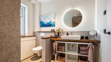 A modern bathroom with a toilet, sink, mirror, and towel storage.